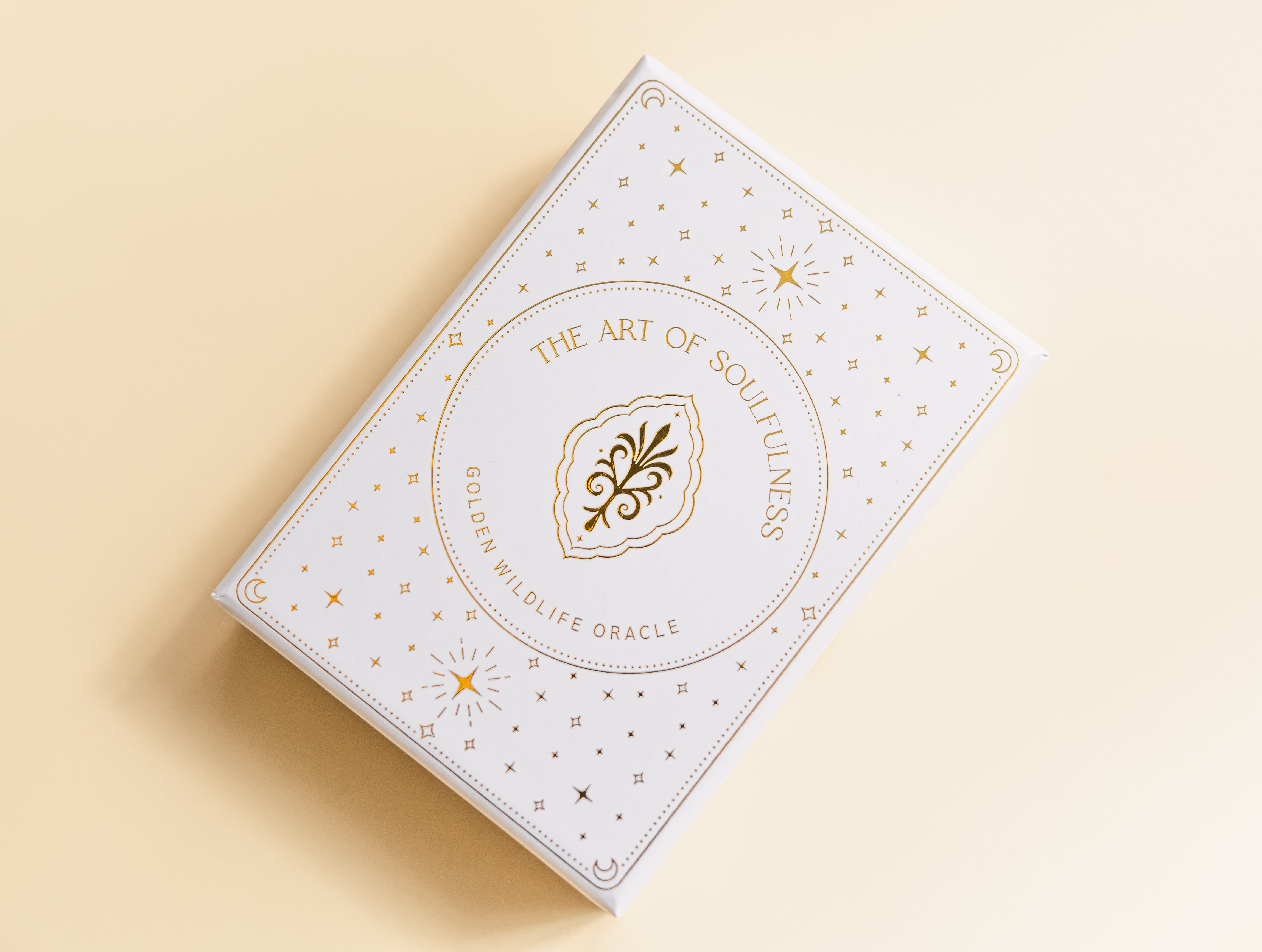 a white oracle deck box with a gold foil design and the text 'the art of soulfulness golden wildlife oracle' on a beige background