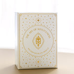 a front view of the gold foiled golden wildlife oracle box on a beige surface with a sheer curtain blurred in the background