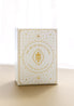 a front view of the gold foiled golden wildlife oracle box on a beige surface with a sheer curtain blurred in the background