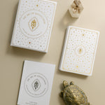 top view of the gold foiled golden wildlife oracle box, deck of cards and guidebook with a brass turtle and smoky quartz point nearby