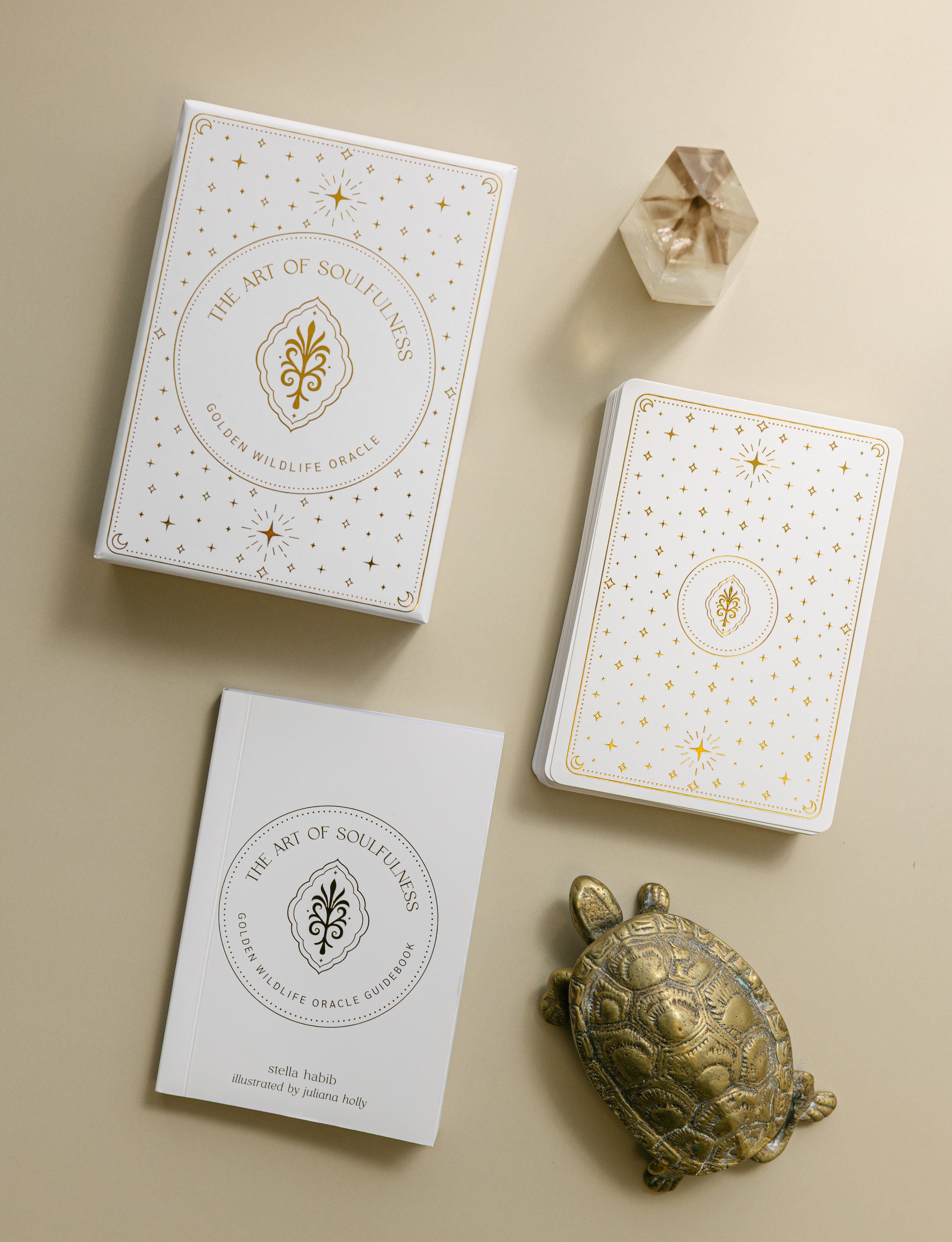 top view of the gold foiled golden wildlife oracle box, deck of cards and guidebook with a brass turtle and smoky quartz point nearby
