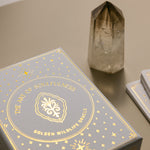 an exterior view of the glimmering gold on the golden wildlife oracle box with a smoky quartz point nearby