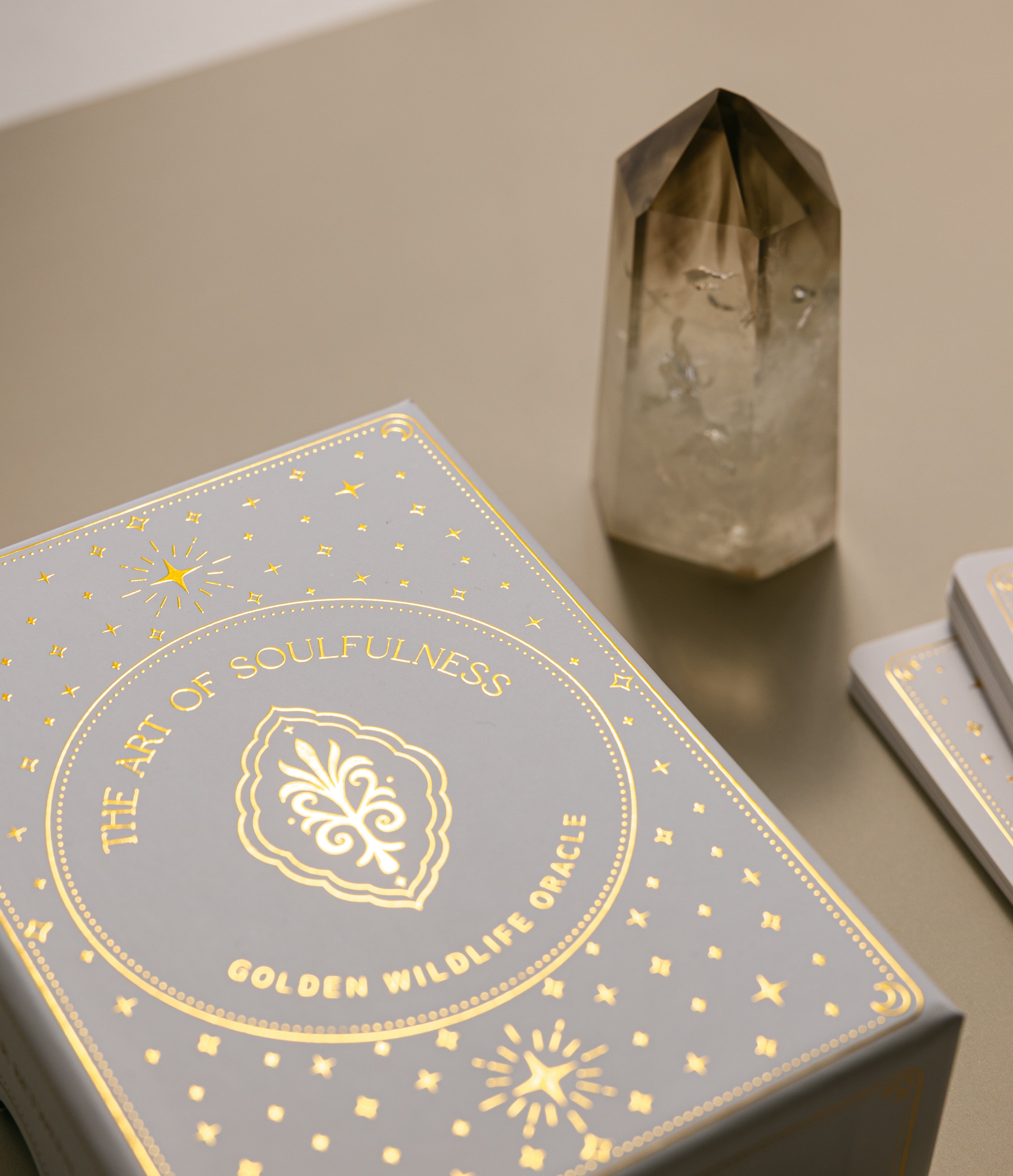 an exterior view of the glimmering gold on the golden wildlife oracle box with a smoky quartz point nearby