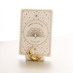 oracle card with a gold foil design that says 'admire your beauty' and features a peacock, held by a matte white card stand decorated with a sculpted gold foil moon and star.