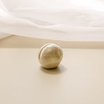 a close-up view of a pearlescent ceramic orb oracle card stand, without an oracle card in it, with a sheer curtain in the background.