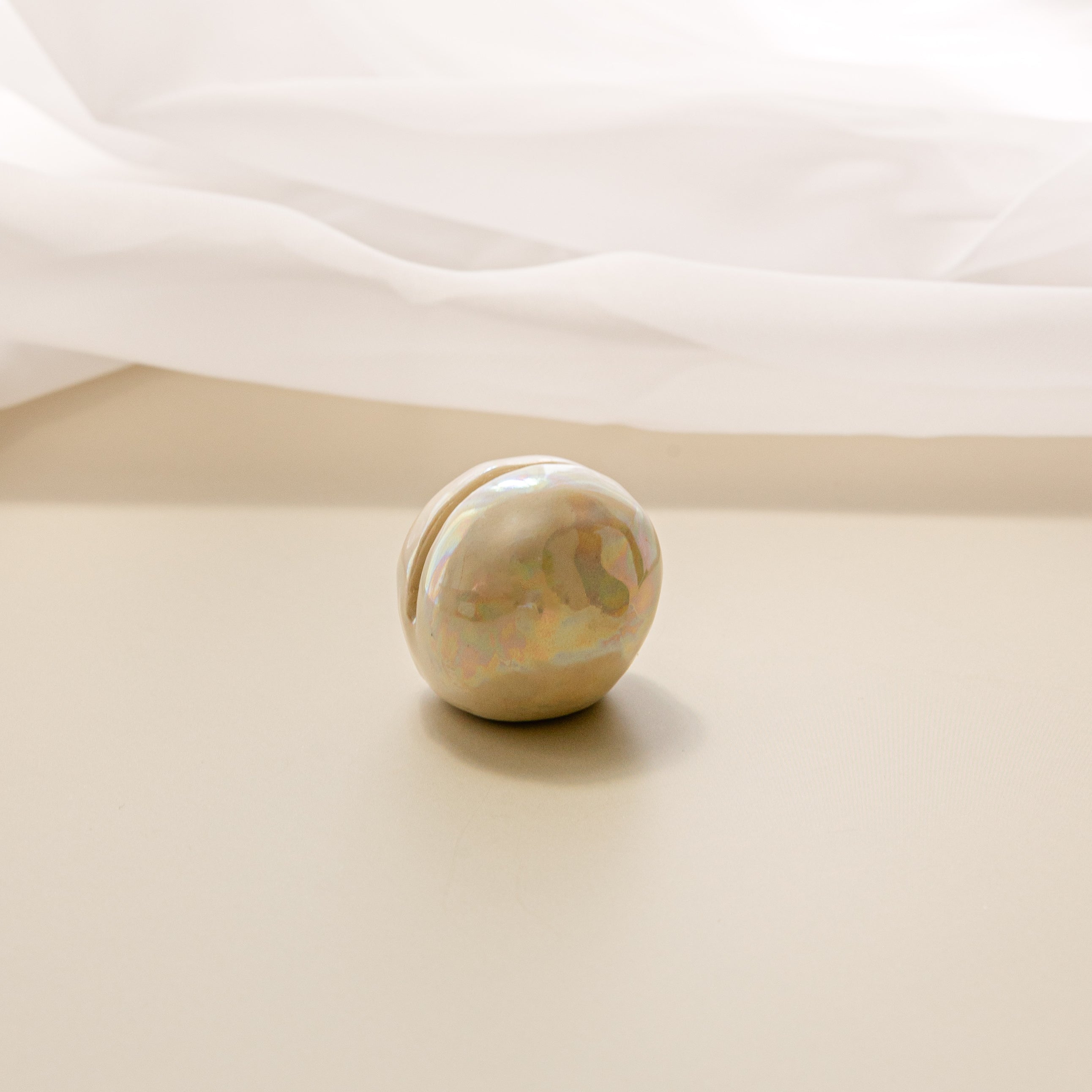 a close-up view of a pearlescent ceramic orb oracle card stand, without an oracle card in it, with a sheer curtain in the background.