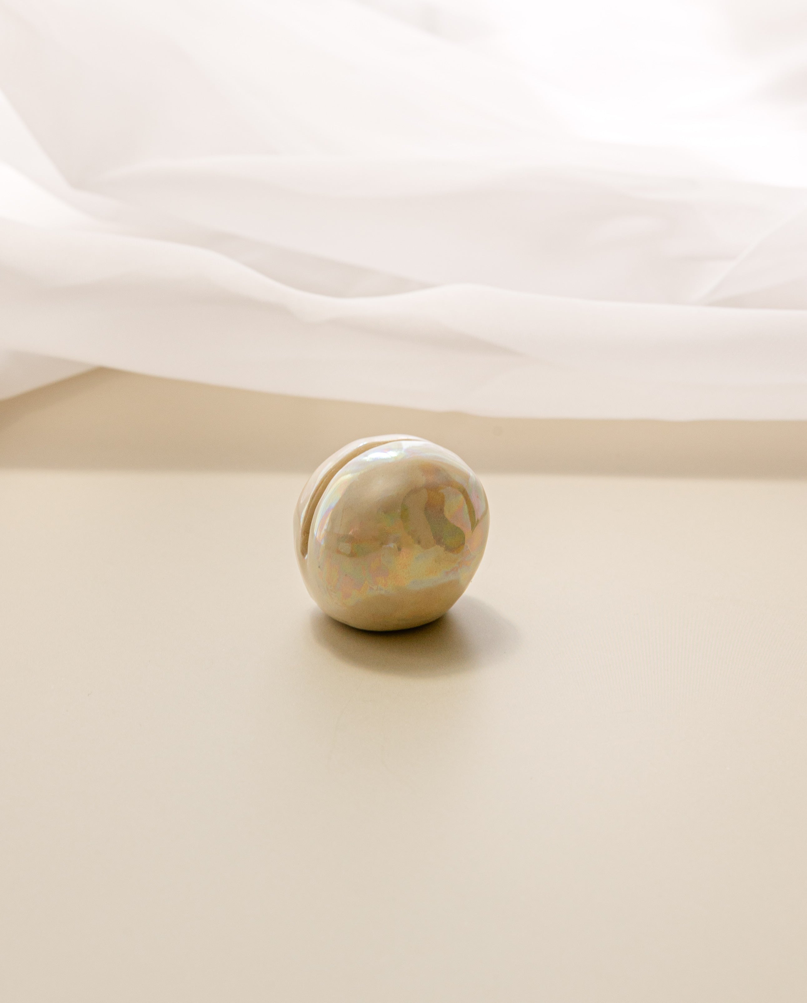 a close-up view of a pearlescent ceramic orb oracle card stand, without an oracle card in it, with a sheer curtain in the background.
