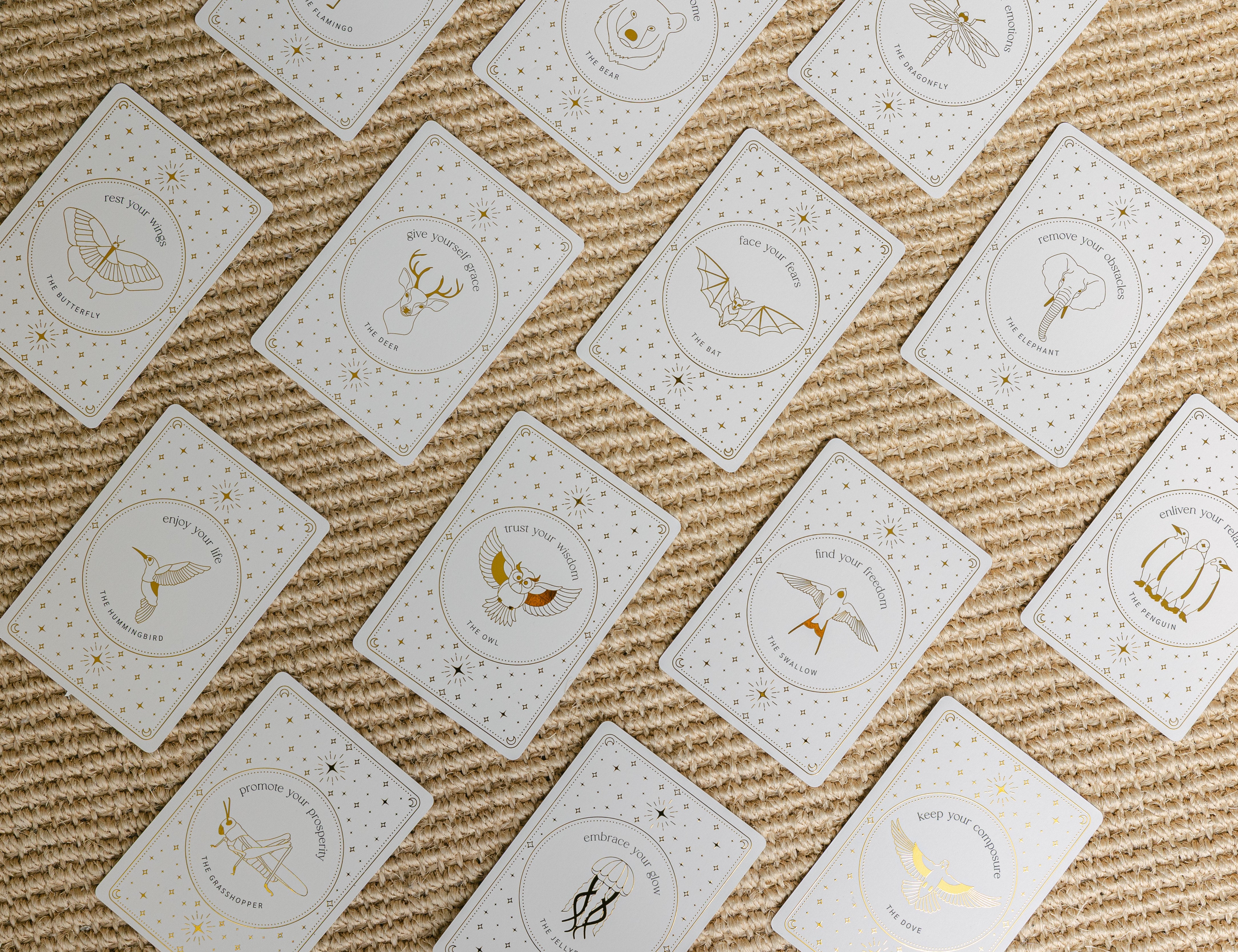 a diagonal, face-up grid of golden wildlife oracle cards on a braided carpet.