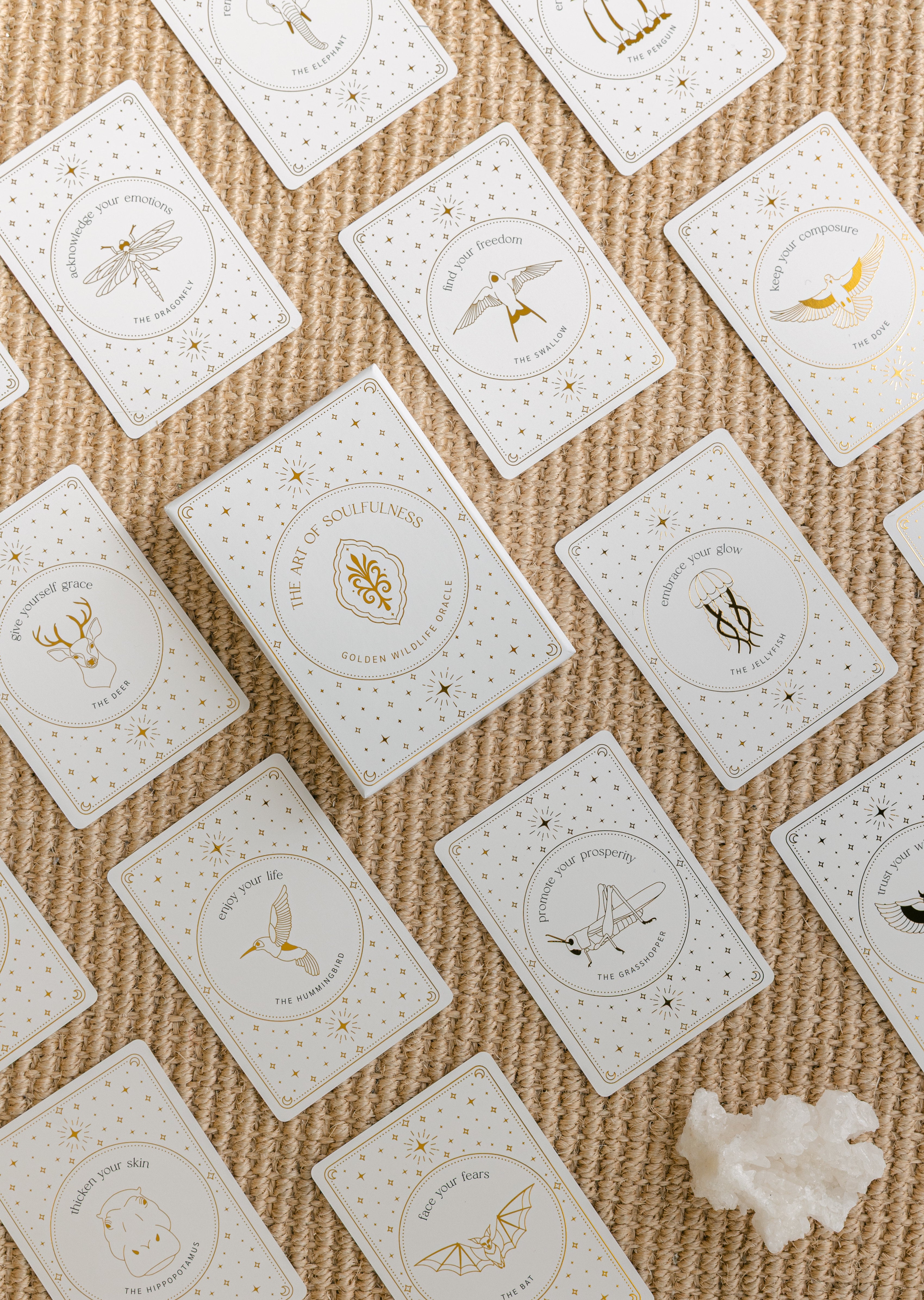 a top view of the golden wildlife oracle box and several of the cards arranged in a face-up grid, with a white aragonite crystal