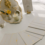 a white matte ceramic oracle card holder with a sculpted moon and star, decorated in gold foil, displaying the hermit crab card from the golden wildlife oracle with a burning candle, ritual shelf, ceramic orb card stand and face down cards from the deck nearby.