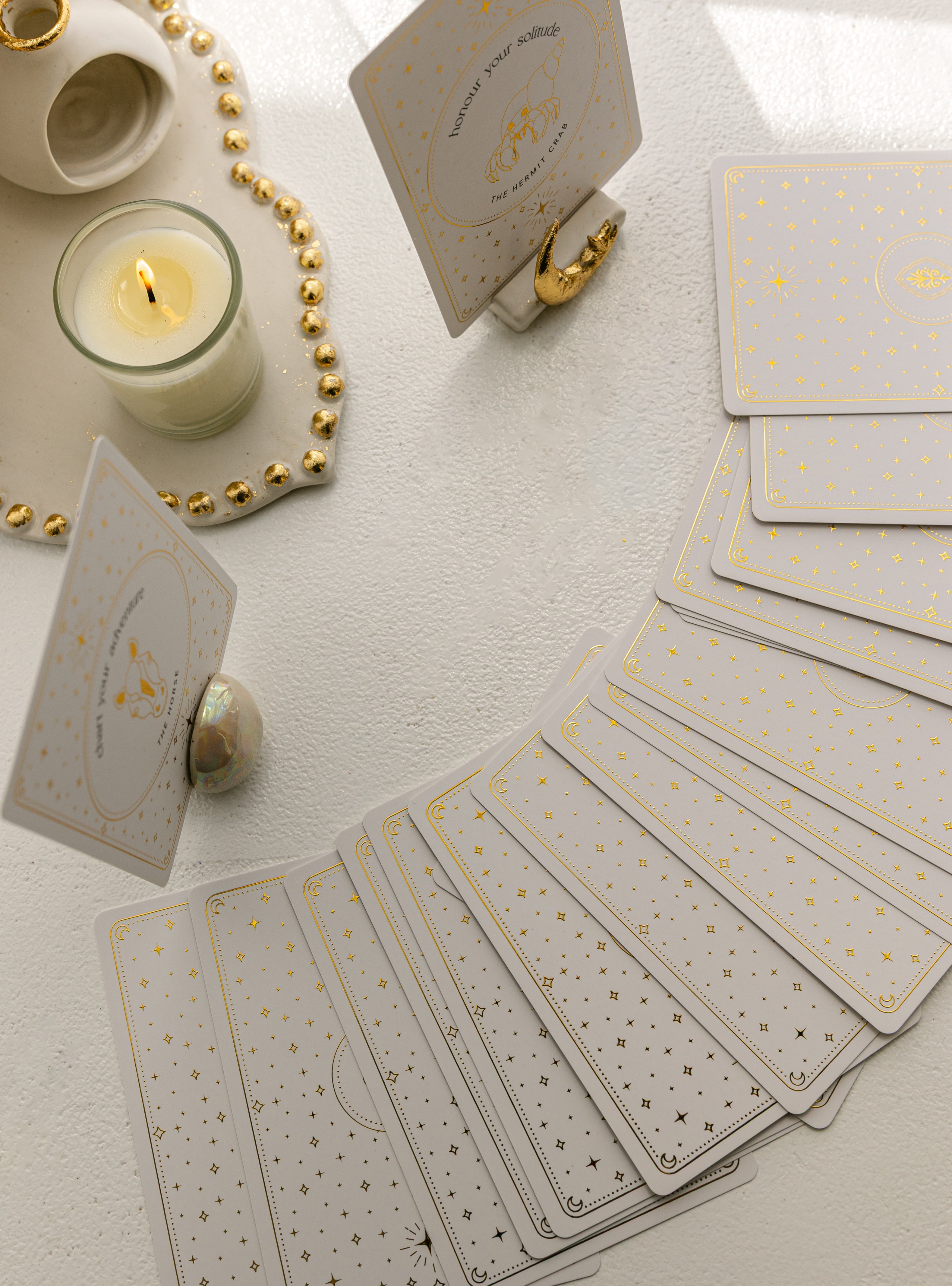 a pearlescent ceramic oracle card holder displaying the horse card from the golden wildlife oracle with a burning candle, ritual shelf, celestial card stand and face down cards from the deck nearby.