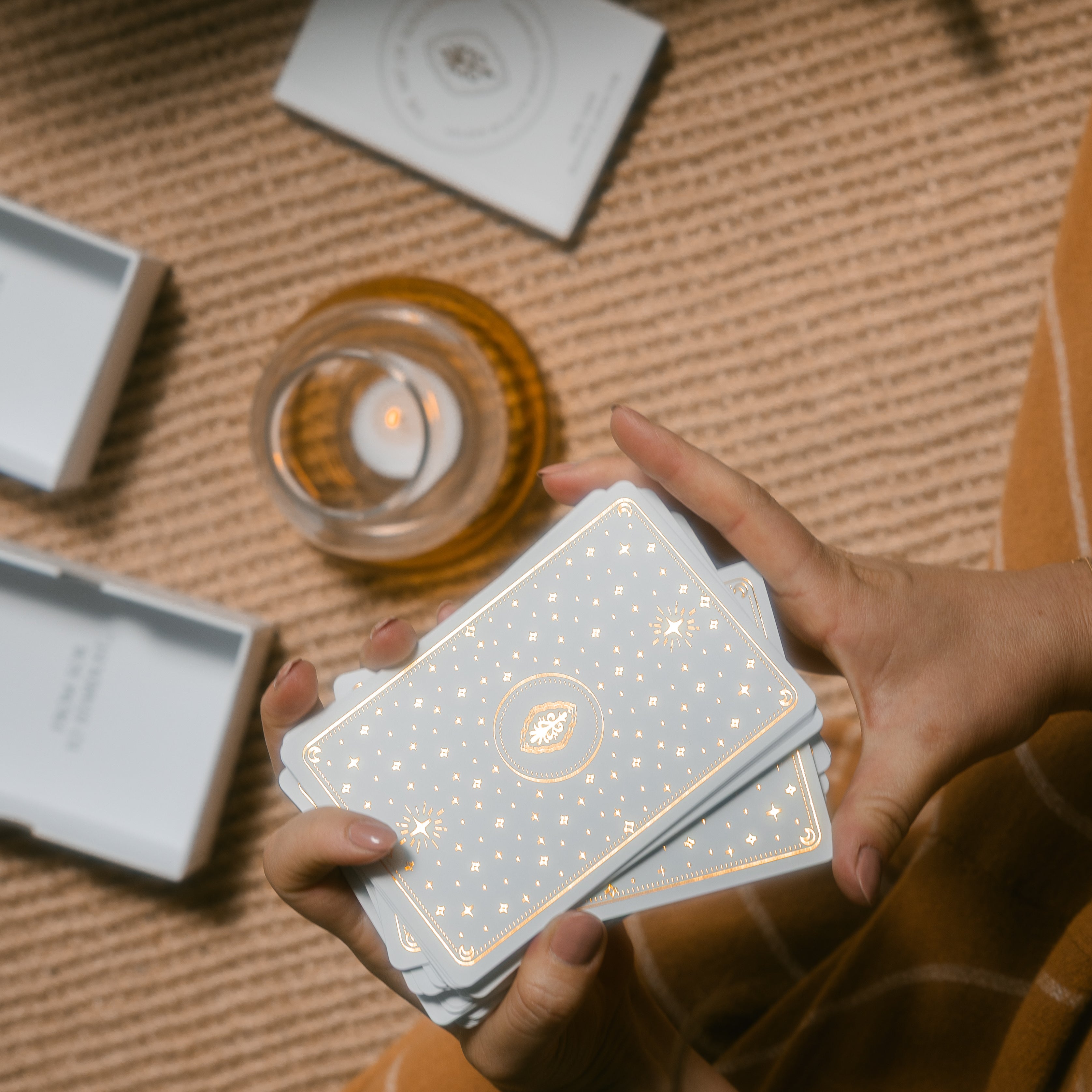 person holding golden wildlife oracle cards with the box, guidebook and a candle in the background, on a braided carpet.