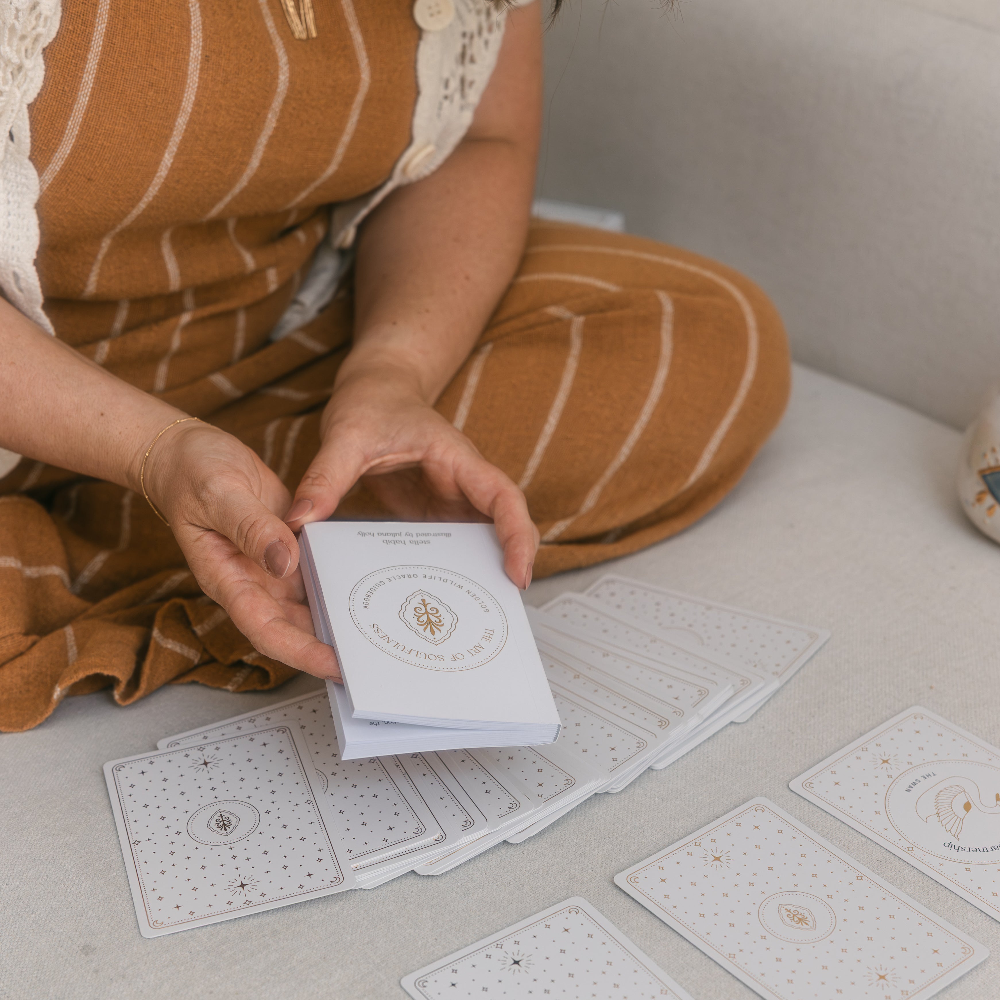 person sitting on a light-coloured couch with a three card golden wildlife oracle spread in front of them, holding the guidebook above it.