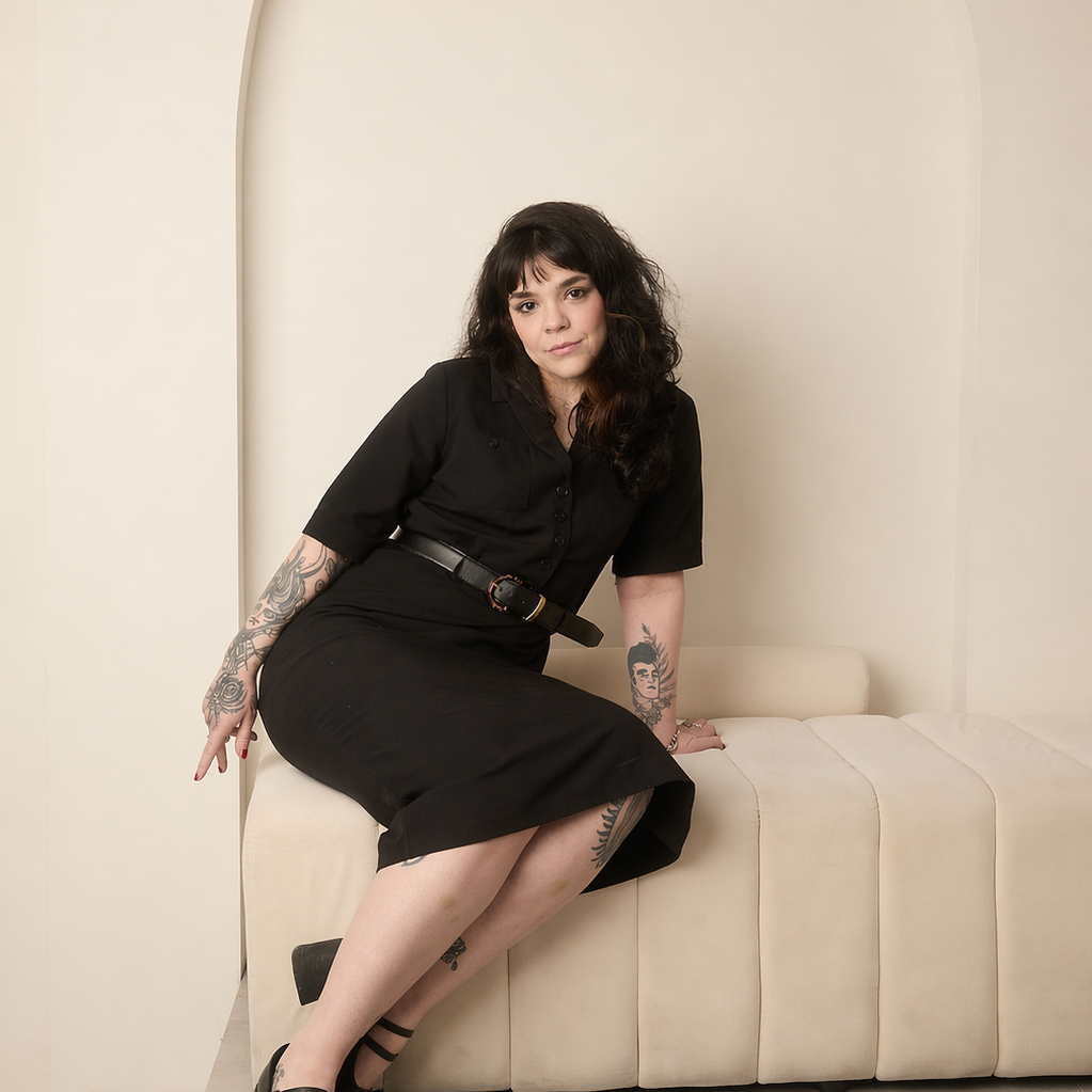 ju wearing a black outfit with black heels, sitting on a modern sofa against a beige wall with arch detailing